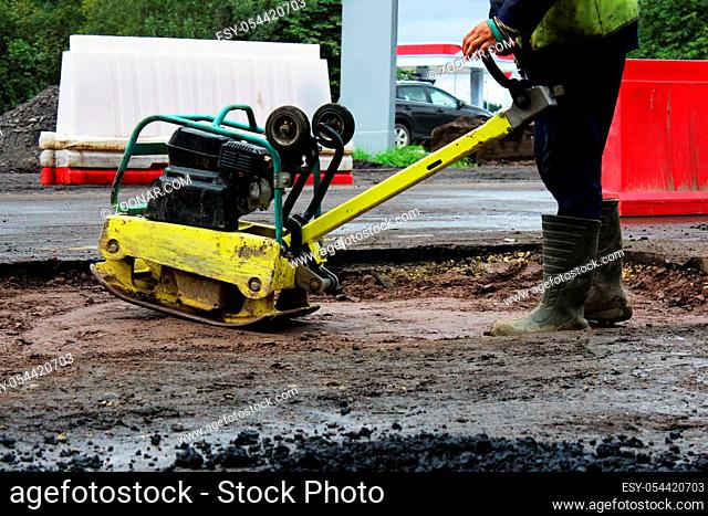 A road construction worker compacts the soil with a compact vibroplate before asphalting a problematic swampy section of the road