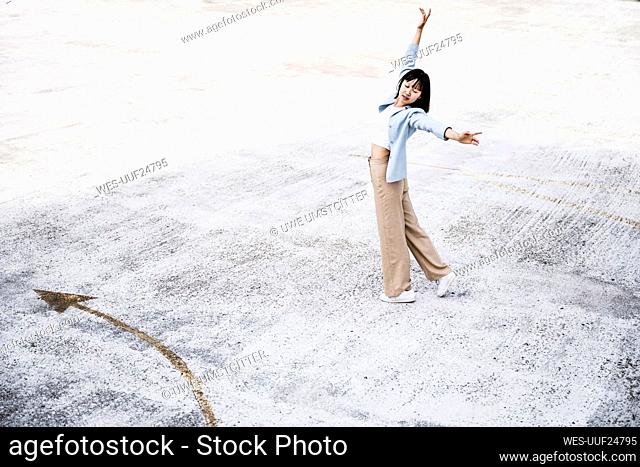 Teenage girl with arms outstretched dancing on parking garage rooftop