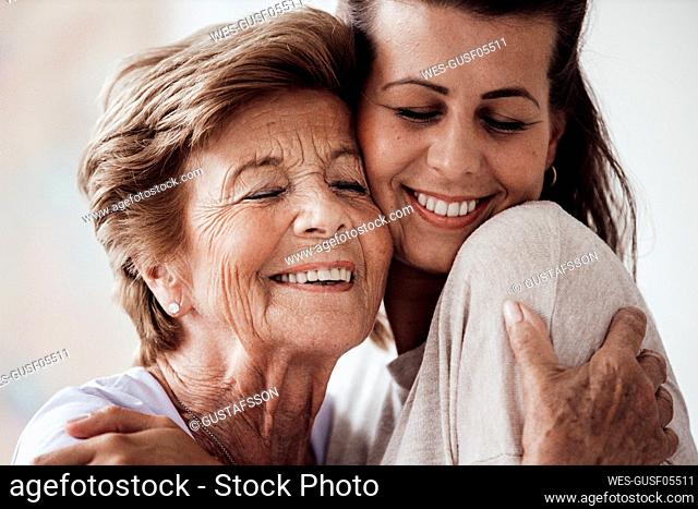 Happy young woman and grandmother hugging each other at home