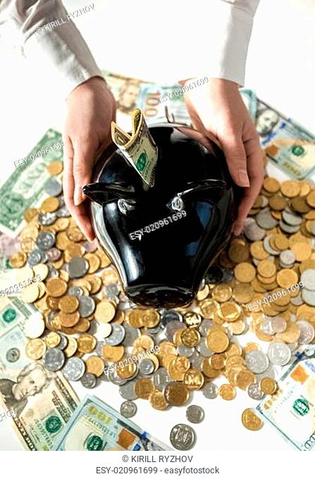 photo of woman holding black pig moneybox on pile of coins