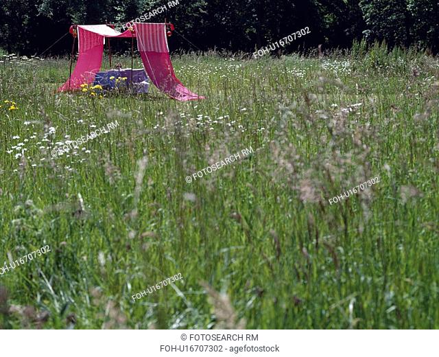 Pink cotton awning in field of long grass in country garden in summer