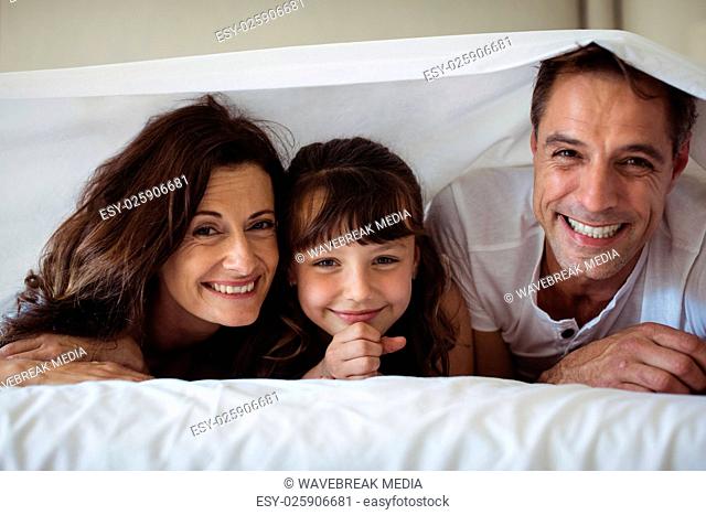 Parents and daughter smiling under the bed sheet