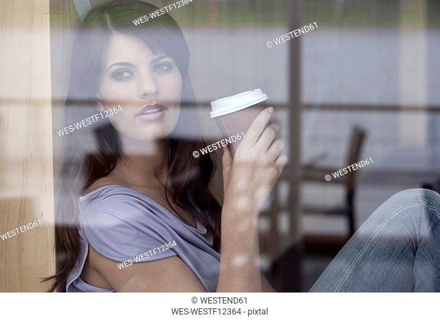 Germany, Cologne, Young woman sitting in window of cafe