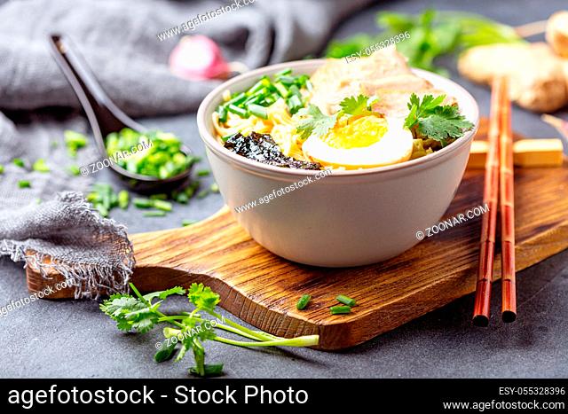 Homemade ramen noodles with meat, egg and green onions in a bowl on a textured gray background, selective focus