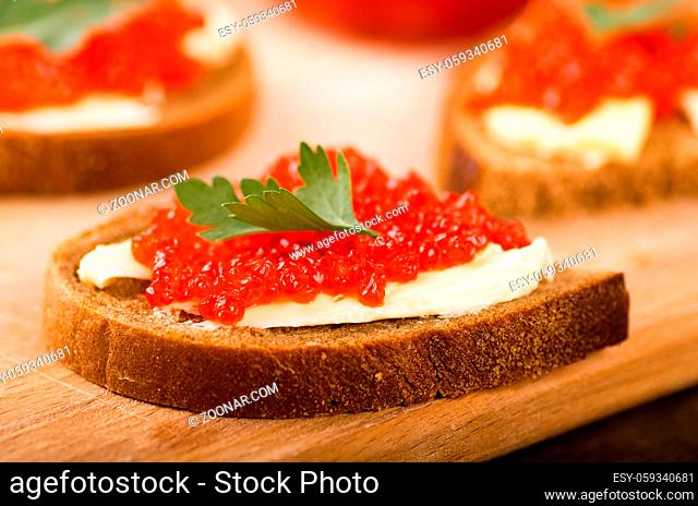 Sandwiches with imitation red caviar and butter on wooden cutting board on wooden table