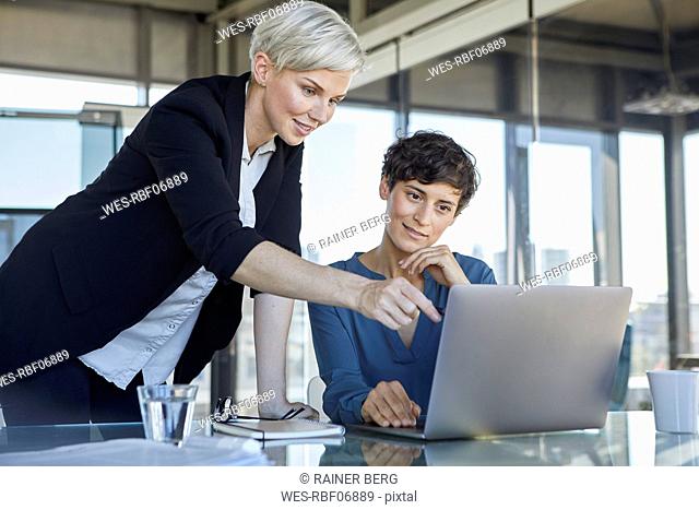 Two smiling businesswomen sharing laptop at desk in office
