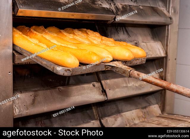 Baker taking out fresh baked bread from the industrial oven
