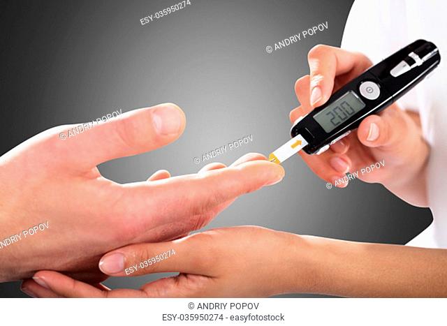 Close Up Of A Person Checking Blood Sugar Level By Glucometer On Gray Background