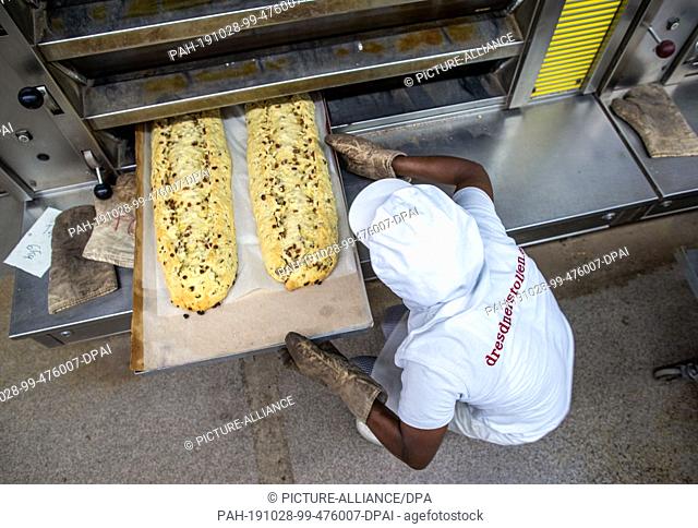 18 October 2019, Saxony, Dresden: Moussa Duale from Guinea pushes a baking tray with two large studs into the oven in the Dresden bakery