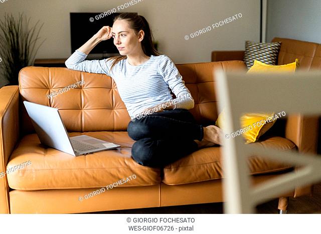 Young woman sitting on couch at home with laptop