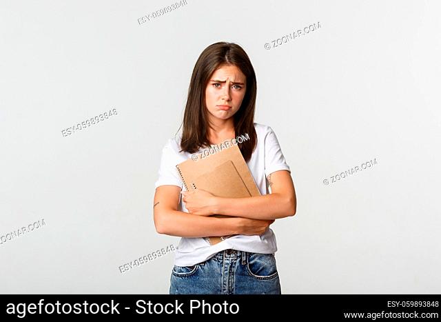 Portrait of gloomy and miserable cute girl with notebooks, frowning and looking sad at camera