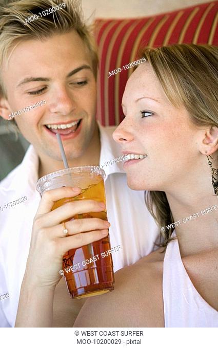 Young couple on sofa woman giving man iced drink close up