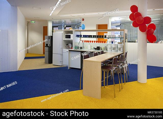 Modern college building, red balloons on a pillar, blue and yellow flooring, and refreshment station, kitchen units and seating