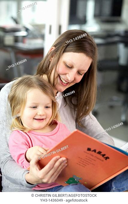 Young mother reading children book to his three year old daughter in the living room