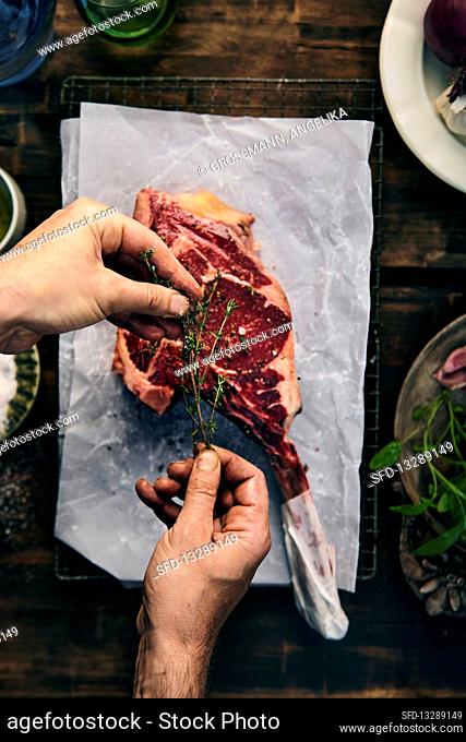 Hands marinating raw tomahawk steak with herbs