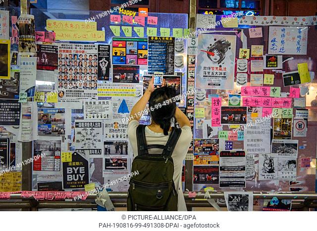 15 August 2019, China, Hongkong: A passer-by photographs handwritten notes and messages from Hong Kongers on a wall of a pedestrian bridge