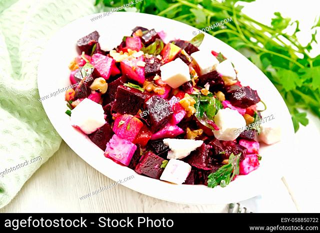 Salad with beets, salted feta cheese, apples, walnuts, parsley, seasoned with balsamic vinegar and olive oil in a plate, green napkin on a wooden board...