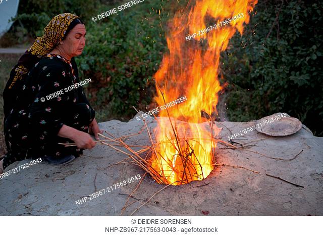 A woman lights the fire in the tandoor outdoor oven for baking bread, early in the morning, Nokhur village, Turkmenistan
