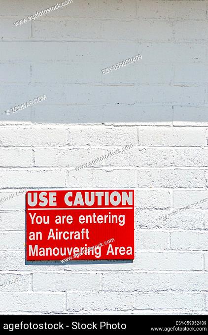 Aircraft manouvering red and white cautionary warning sign hung on painted brick wall