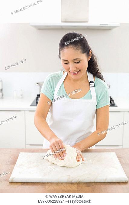 Smiling woman kneading dough in the kitchen