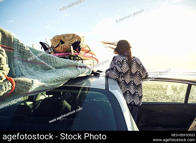 Back view of woman with car on the beach looking to the sea, Tafedna, Morocco
