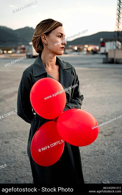 Beautiful woman holding red balloon while looking away