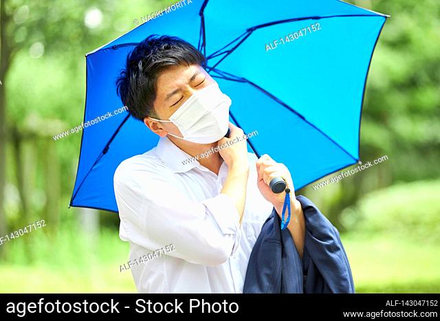 Young Japanese businessman wearing mask in the hot Summer downtown Tokyo