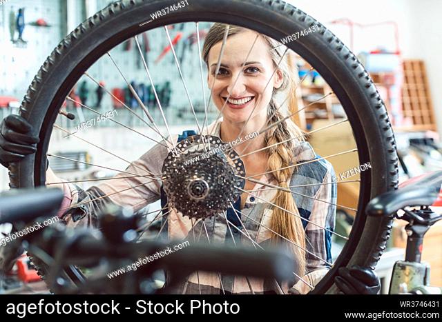 Very happy bike mechanic woman looking through the wheel of bicycle