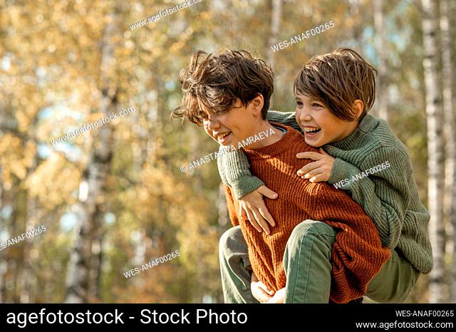 Happy boy giving piggyback ride to brother in park
