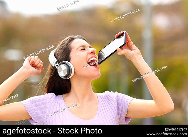 Happy teen singing in the street using phone as mic