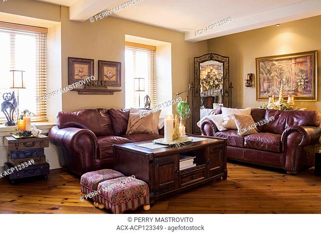 Burgundy leather sofas and wooden coffee table in living room inside an old renovated (circa 1840) Canadiana cottage style home, Quebec, Canada