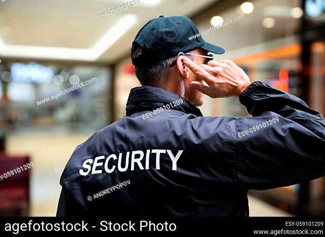 Rear view of mature security guard listening to earpiece against building