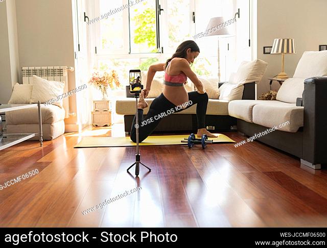 Pregnant woman doing stretching exercise recording tutorial through mobile phone at home