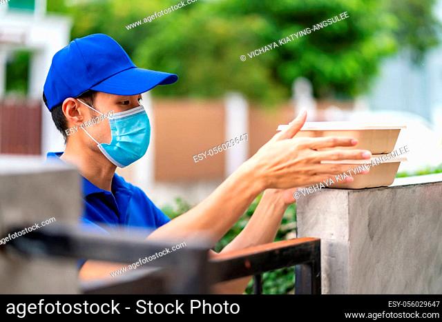 Asian deliver man with face mask in blue shirt handling food boxes and put in on the fence post of customer house as contactless food delivery