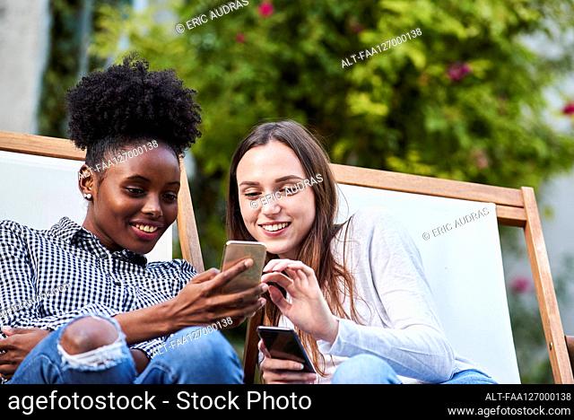 Smiling young friends using smartphones in park
