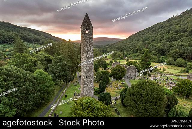 Aerial of the Round Tower looking through the window to the sun rising over the hills at Glendalough (or The valley of the Two Lakes) the site of an early...