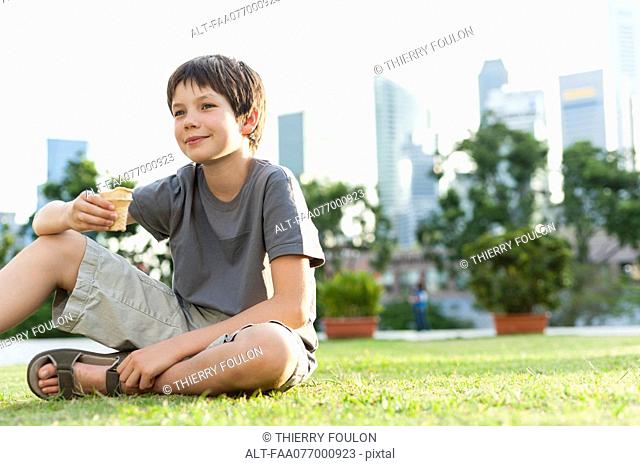 Boy sitting on grass in park, city skyline in background