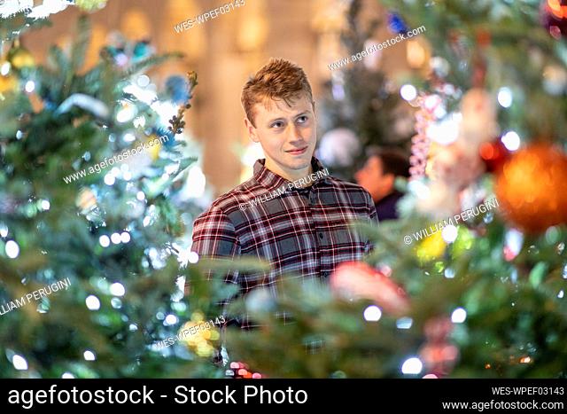 Young man looking at illuminated Christmas tree and lights in city