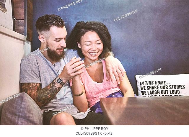 Multi ethnic hipster couple in cafe laughing, Shanghai French Concession, Shanghai, China