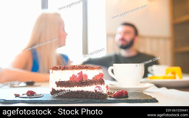 Sweet cake in front of couple sitting in a cafe enjoying conversation, close up