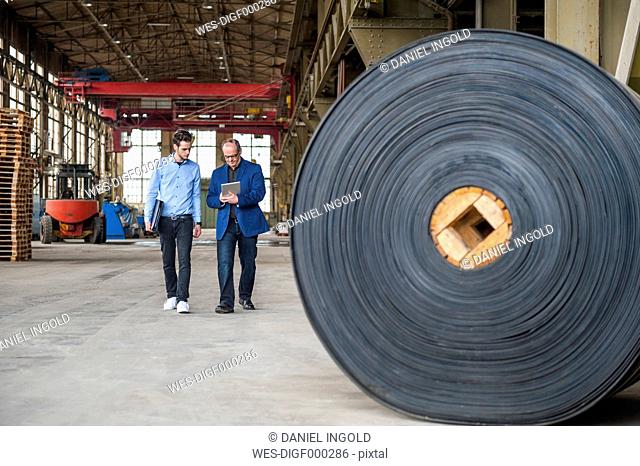 Two men walking in factory hall with rolls of rubber