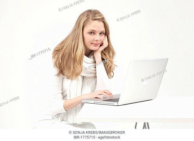Blonde young woman dressed in white working on a laptop