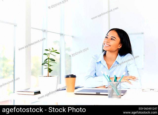 Smiling pretty black businesswoman posing at her desk in a bright modern office looking to copy space. business success concept