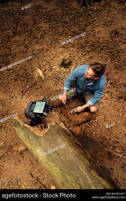 Male biologist taking dirt samples on land in forest