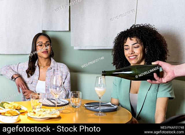 Male waiter serving drink in glass by businesswomen at restaurant