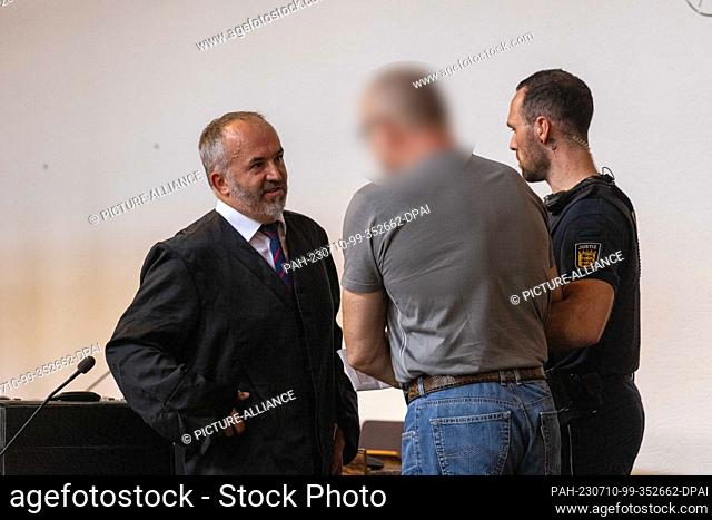 10 July 2023, Baden-Württemberg, Freiburg: A defendant (M) talks to his defense attorney (l) while a court official (r) holds him by the arm