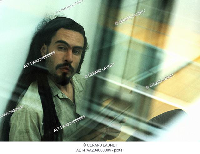 Man sitting looking at camera, view through glass