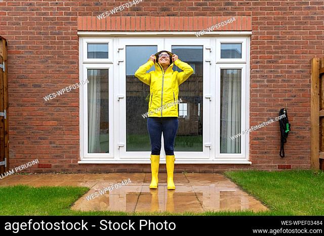 Woman wearing raincoat looking up while standing in back yard during rainy season