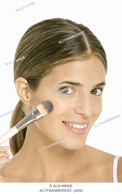 Woman applying blush, smiling at camera, close-up