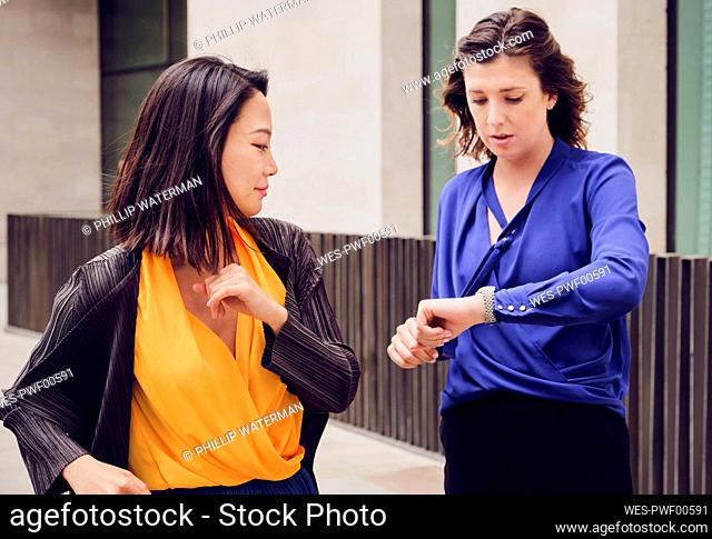 Businesswoman with colleague checking time standing on footpath